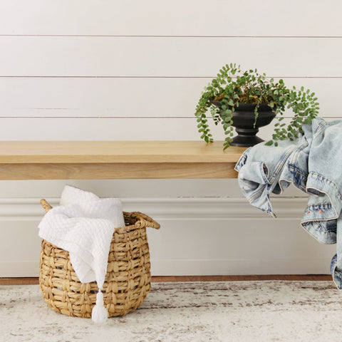 Wooden bench sitting in front of a wall. There is a plant and denim jacket styled on the bench.