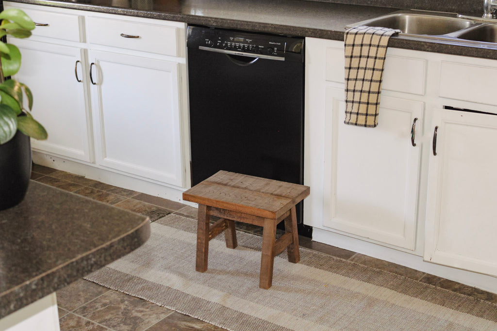 Rustic step stool in a kitchen. The step stool is sitting in front of the kitchen sink.