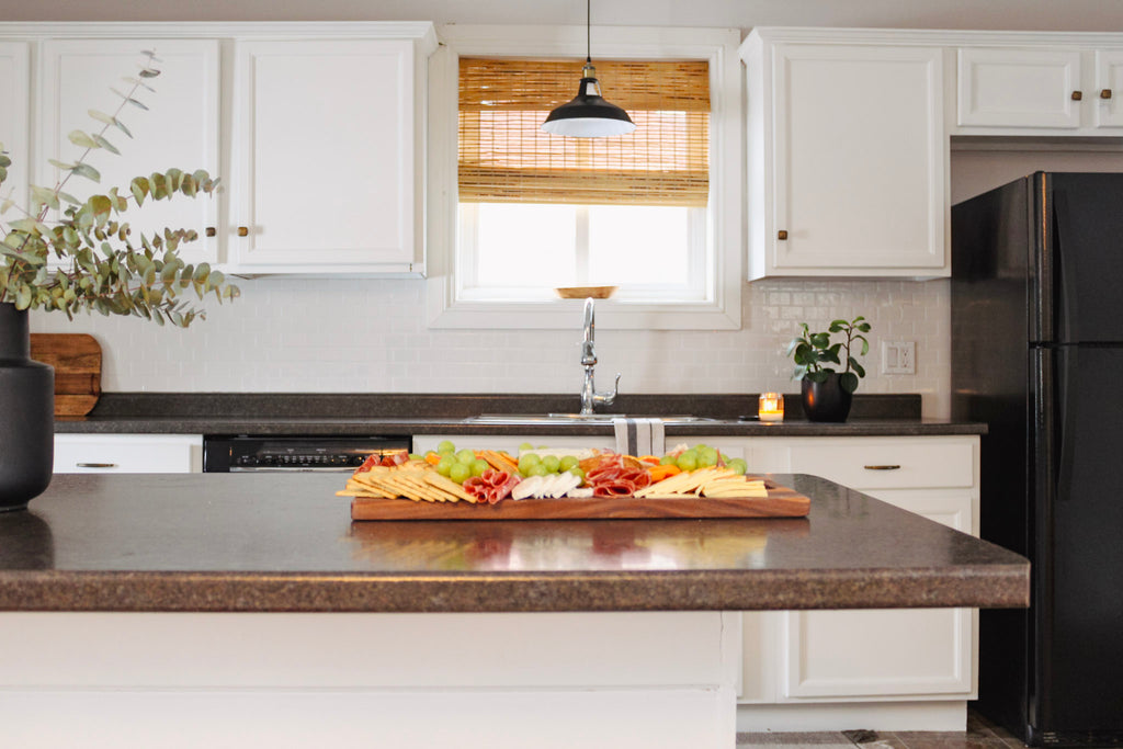 Styled image of the board being used as a charcuterie board. The charcuterie board is sitting on a kitchen island.  