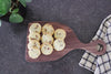 Wooden walnut cutting board sitting on a counter with some chocolate chip cookies on it.