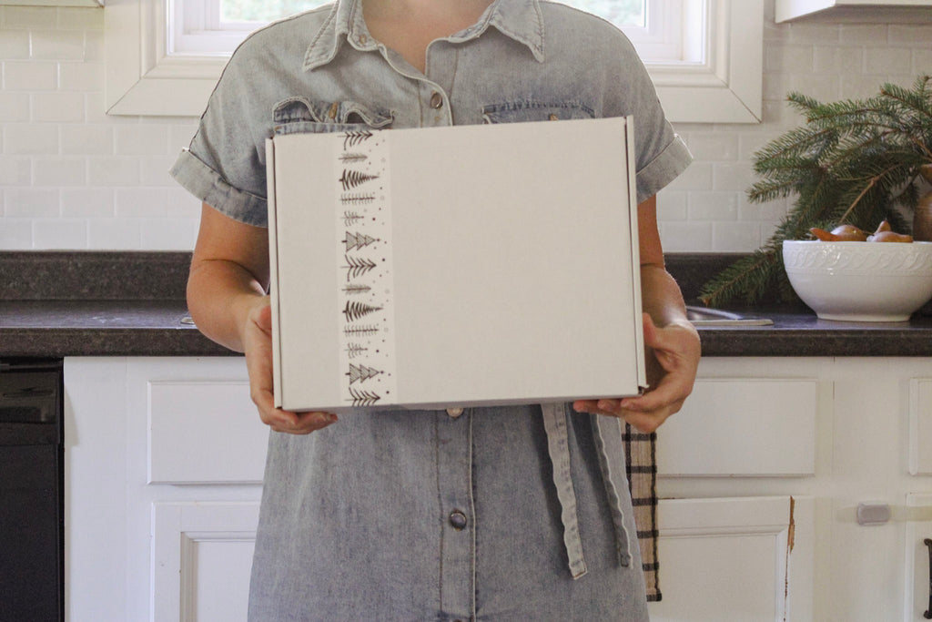 A person holding a white box with some white tape with black pine trees on it.