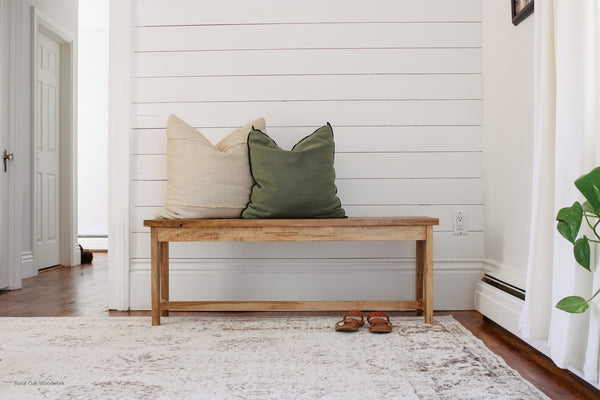 Homestead wormy maple bench styled against a white wall with a green and tan throw pillow sitting on top of it.