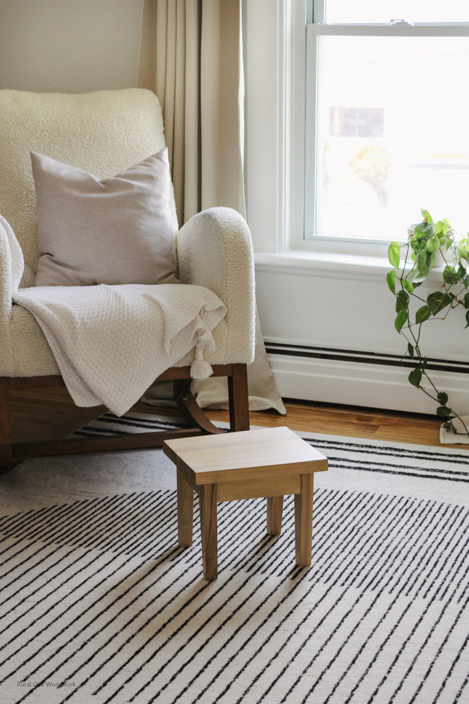 Step stool styled in front of a cream rocking chair. There is a window behind the rocking chair with a plant sitting on it.