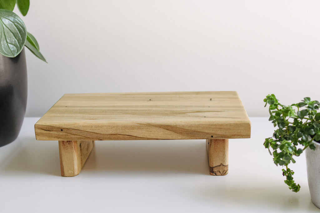 Wooden tray sitting on a flat surface with some greenery surrounding it.