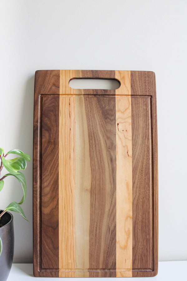 Wooden cutting board sitting upright against  a wall. There is a potted plant on the one left side.