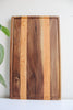 Wooden cutting board set upright against a wall. On the left side of it is some greenery.