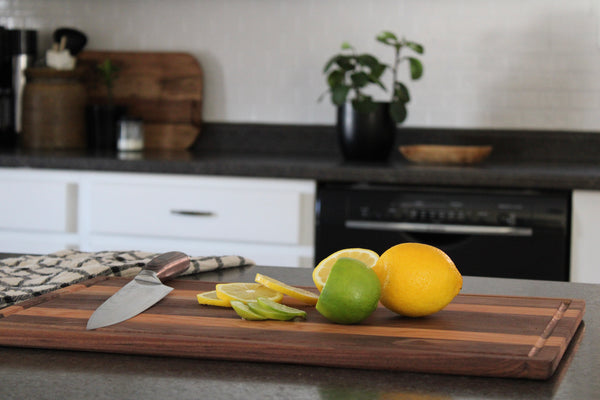 Wooden cutting board sitting on kitchen counter, on the cutting board is a lemon and lime. A part of the lemon and line has been sliced.