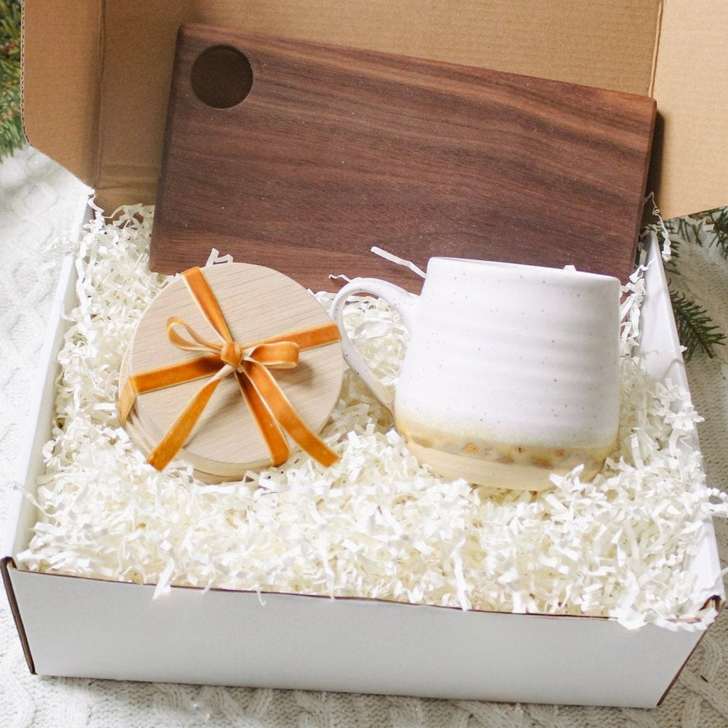 gift box, in the box is a set of wooden coasters a pottery mug and a wooden cheese board.