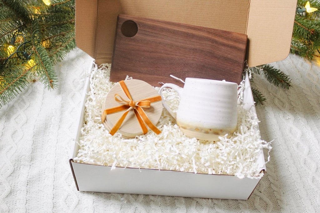 Christmas gift box, in the box is a set of wooden coasters a pottery mug and a wooden cheese board.