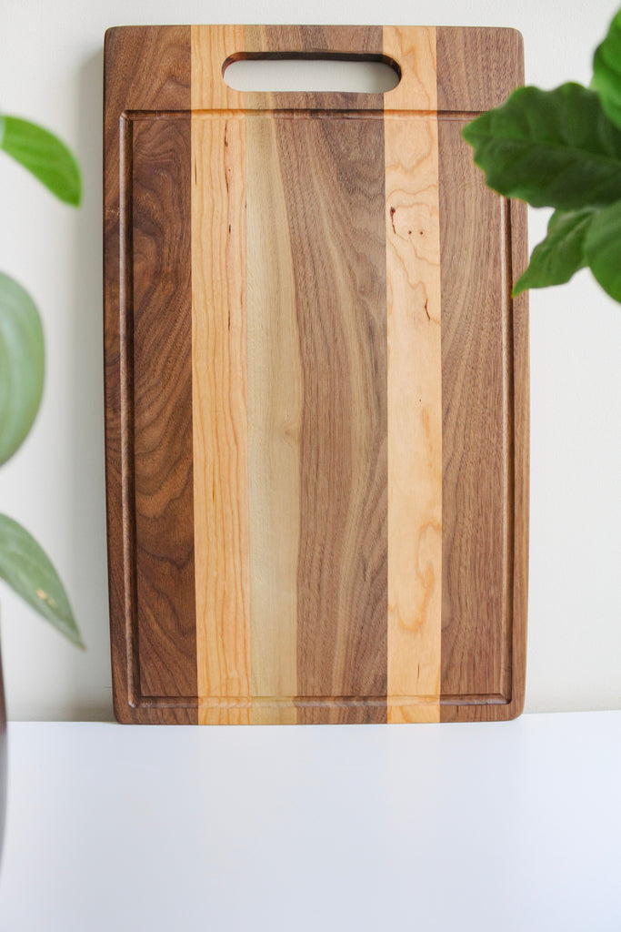 Wooden cutting board standing up against the wall with  some indoor plants on either side of it.