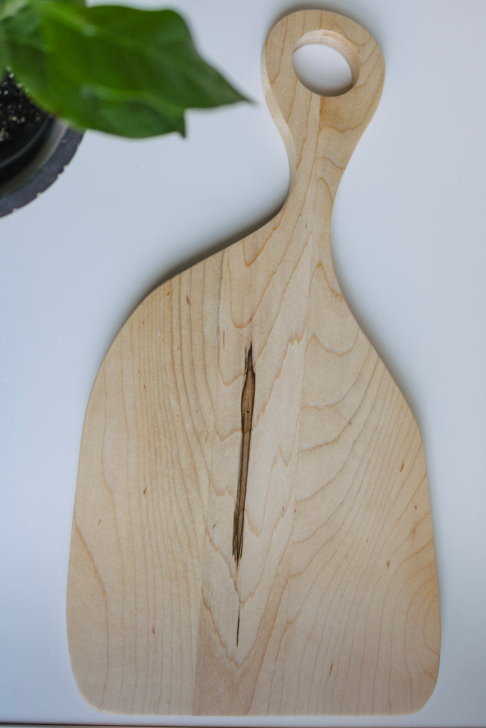 Wooden cutting board laying on a flat surface with a plant in the one corner.